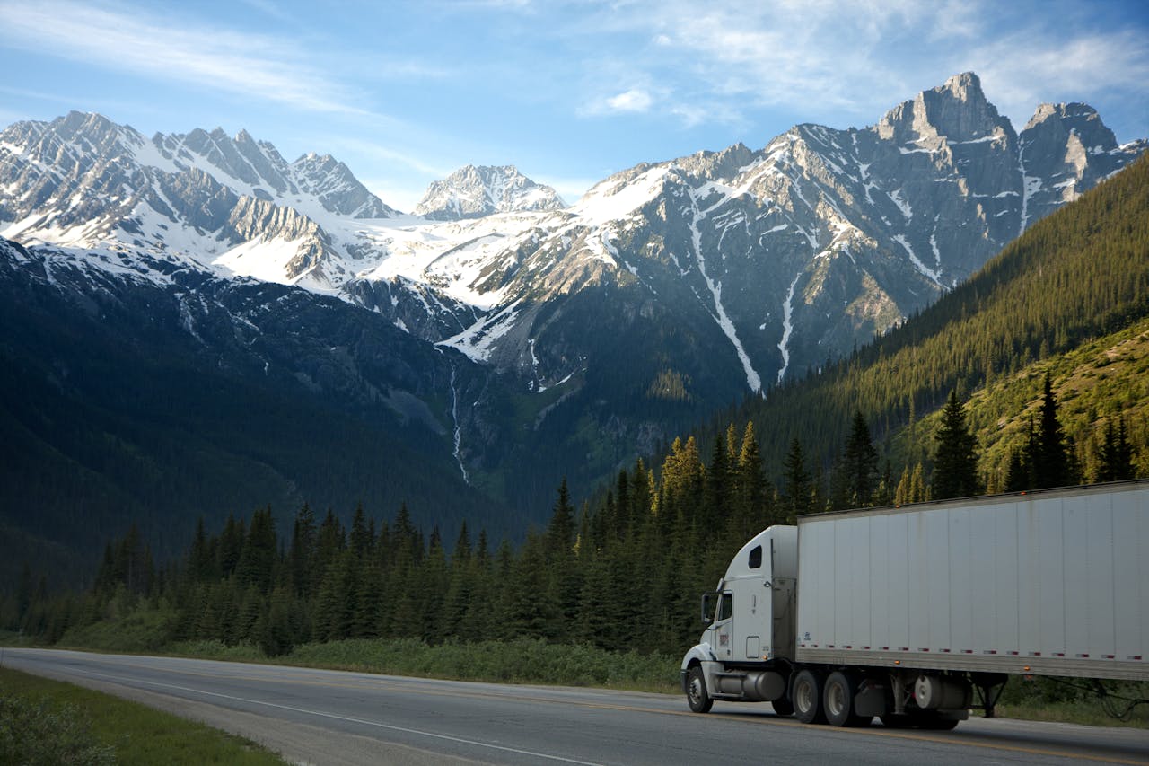 services-img A semi-truck travels along a highway with snow-capped mountains in the background.